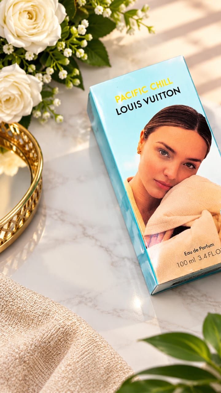 Louis Vuitton Pacific Chill Eau de Parfum box placed on a marble surface with white roses, a gold tray, and beige fabric props around it.