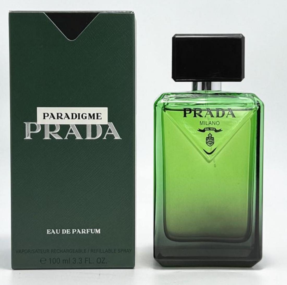 Prada Paradigme Milano Eau de Parfum, showing the green gradient glass bottle with a black cap next to its dark green textured packaging box.