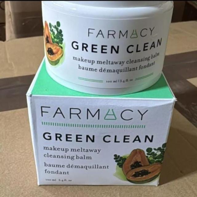 A white jar of FARMACY Green Clean makeup meltaway cleansing balm sits on top of its white and mint green retail box, photographed on a cardboard surface.