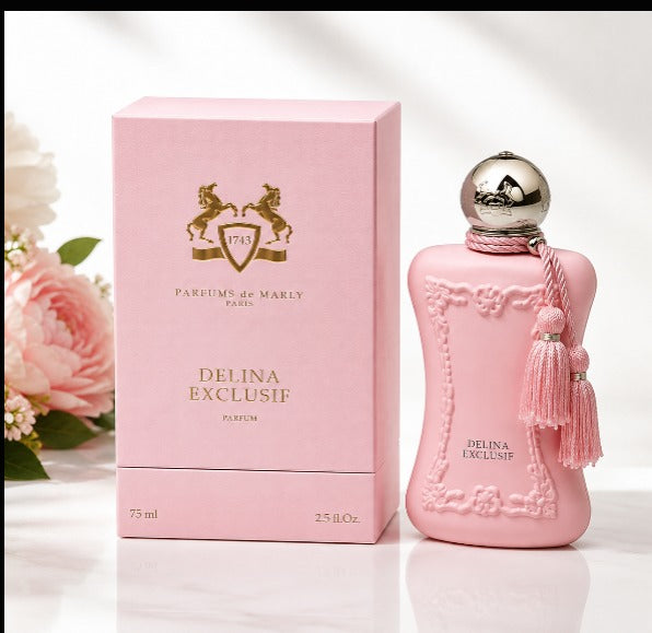 Pink perfume bottle and matching pink box for Parfums de Marly Delina Exclusif, shown on a clean white surface with soft floral props at the side.