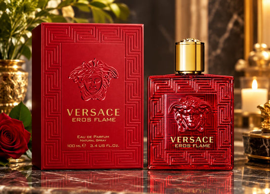 Versace Eros Flame Eau de Parfum bottle and its red packaging box, displayed on a reflective marble surface with candles and roses in the background.