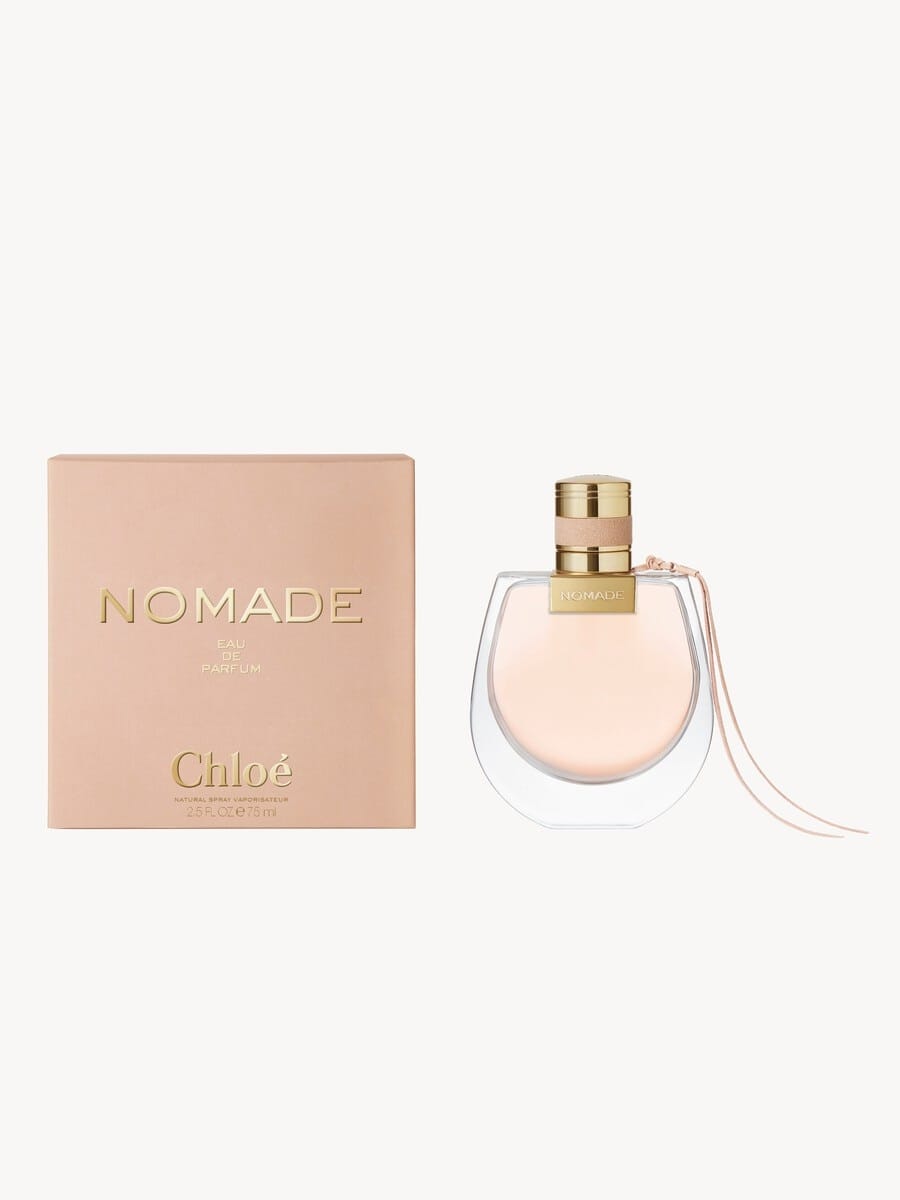Chloë Nomade Eau de Parfum bottle with a gold cap next to its peach-colored packaging box on a light off-white background.