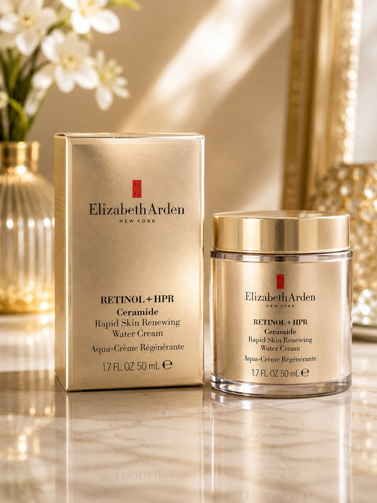 Elizabeth Arden Retinol + HPR Ceramide Rapid Skin Renewing Water Cream shown with its metallic gold box and matching jar on a reflective surface, with a softly blurred warm-toned interior background.